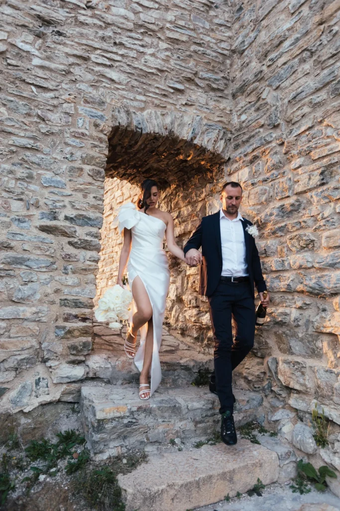 A couple in wedding attire holding hands while walking through a stone archway at Medvedgrad Zagreb.
