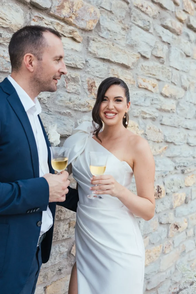 A young couple celebrating their elopement at Medvedgrad, Zagreb, holding champagne glasses against a historic stone wall backdrop.