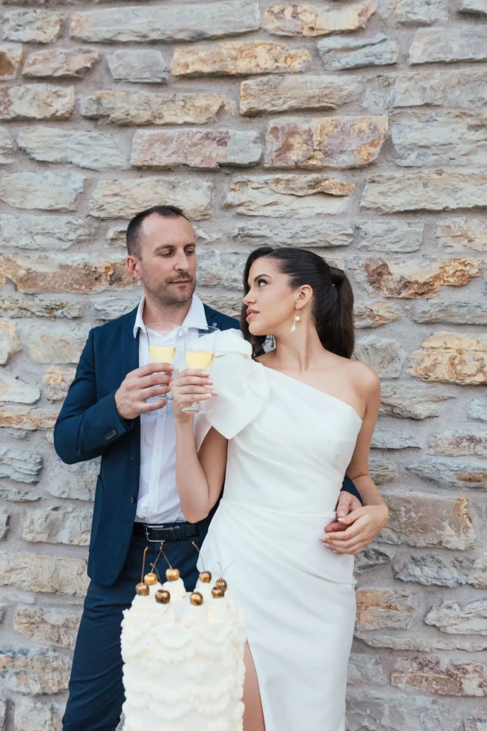 A couple celebrating their elopement at Medvedgrad in Zagreb, holding champagne glasses beside a beautiful wedding cake.