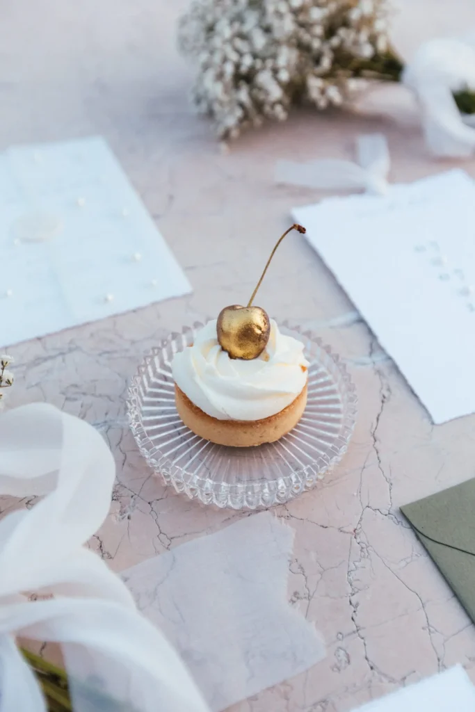A golden cherry topped cupcake on a crystal plate, surrounded by elegant wedding stationery, symbolizing a sweet moment during an elopement at Medvedgrad Castle in Zagreb.