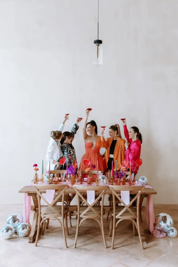 A group of ladies celebrating, raising their glasses for a toast at a table adorned with colorful decorations.